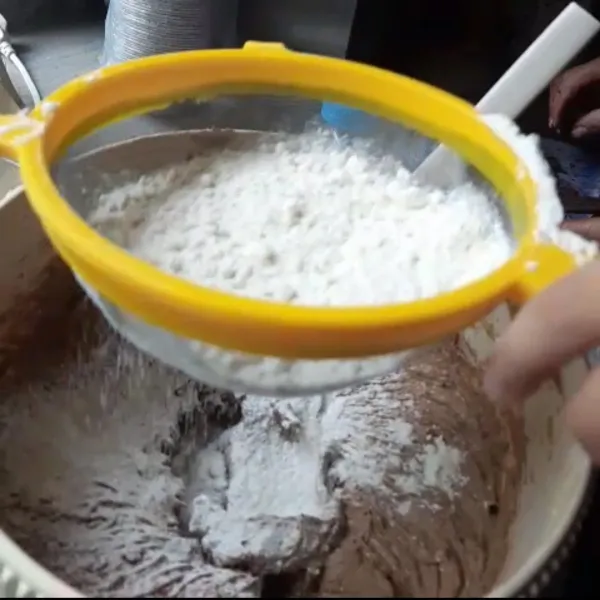 Setelah semua bahan step 1 tercampur rata, tambahkan tepung terigu perlahan-lahan. Aduk dengan menggunakan spatula. Tambahkan juga baking powder, baking soda dan coklat bubuk.