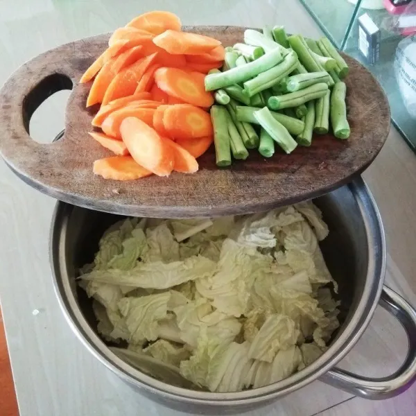 Kupas atau kerok kulit wortel dan iris menyerong. Potong-potong buncis. Pisahkan bongkol serta daun sawi, potong sesuai selera. Lalu cuci bersih semua sayuran. Tiriskan.