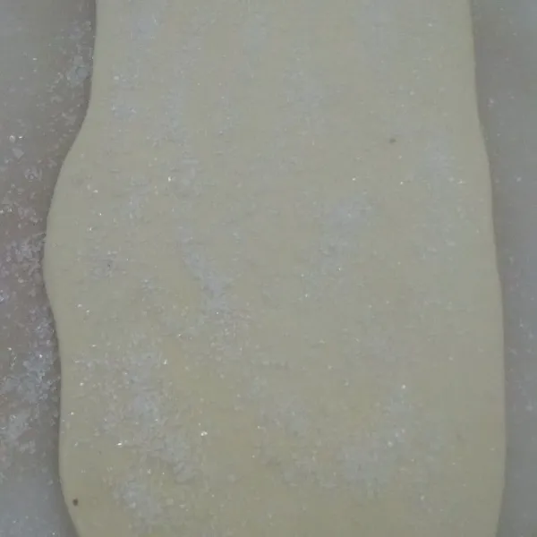 Taburkan setengah gula ke papan secara merata lalu beri adonan pastry dan taburi lagi dengan gula sisanya. Rolling di atas gula agar gula menempel di adonan puff pastry.