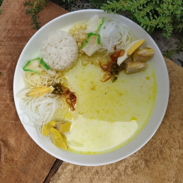 Tata soto. Masukkan soun, tauge, kol, seledri, bawang goreng, telur rebus dalam wadah. Lalu siram dengan kuah soto. Beri taburan dengan bubuk koya. Soto lamongan khas soto jawa siap dinikmati.