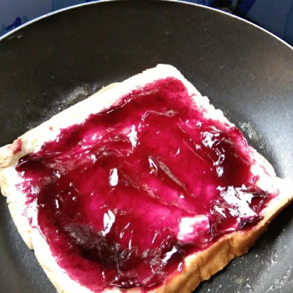 Tambahkan selai bluberry di atas roti lalu ratakan.