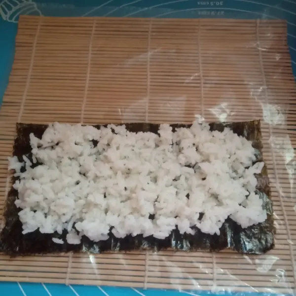 Siapkan sushi mat alasi dengan plastik,taruh nori lalu nasi sambil di ratakan tipis sisakan pinggir nori sedikit.