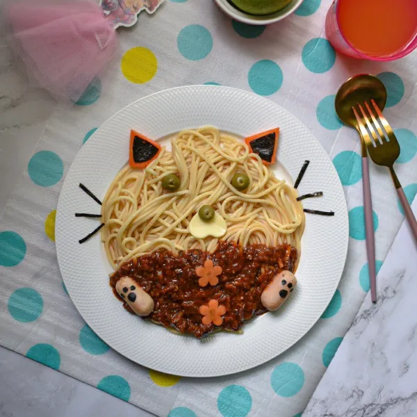 Tata spaghetti di atas piring, beri saus bolognese, dan hias dengan karakter Garfield.