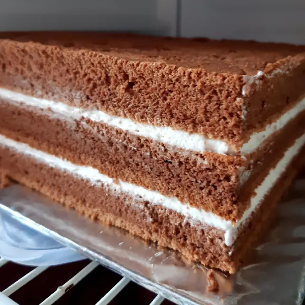 Setelah dingin, beri whipping krim pada setiap layer cake, kikis bagian tepian cake agar rapi, masukkan kulkas biarkan whipping krim set.