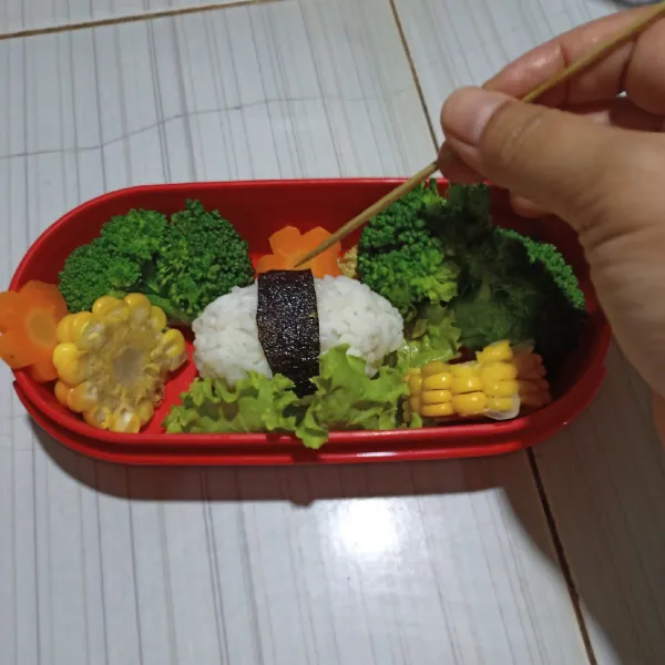 Tata nasi putih kepal di atas selada. Gunting Nori lalu tempelkan di nasi putih menggunakan tusuk gigi.