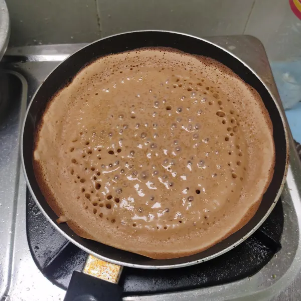 Panaskan teflon, masukkan separuh adonan dan basahi bagian pinggir teflon. Gunakan api sedang cenderung kecil agar bagian bawah tidak cepat gosong. Tunggu bagian permukaan martabak sedikit basah dan berlubang-lubang, taburkan sedikit gula putih. Tutup teflon hingga martabak matang sempurna.