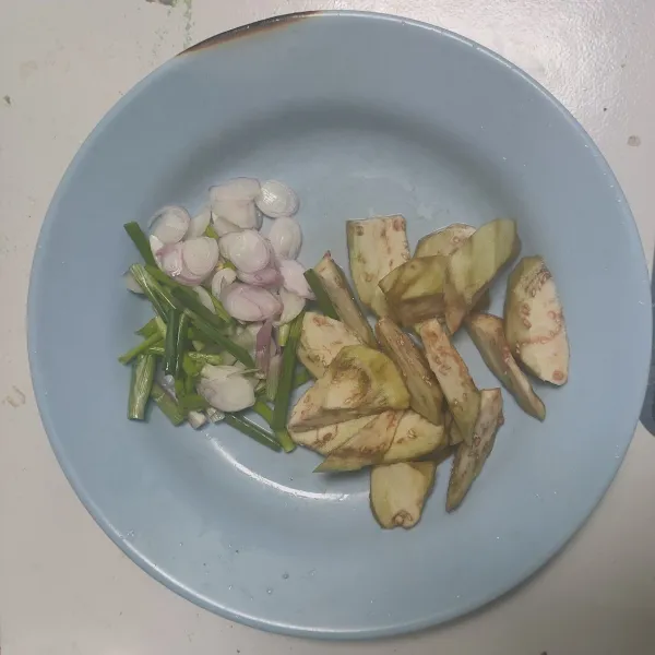 Kupas terong, cuci bersih dan potong serong. Potong daun bawang.