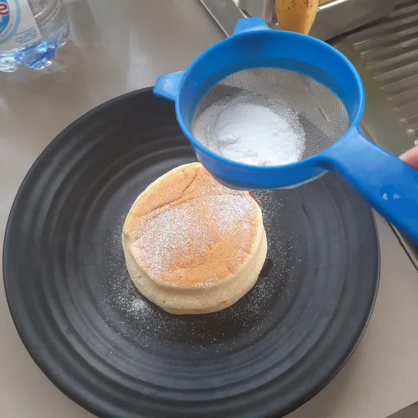 Sajikan pancake di atas piring kemudian beri taburan gula halus dan potongan buah.