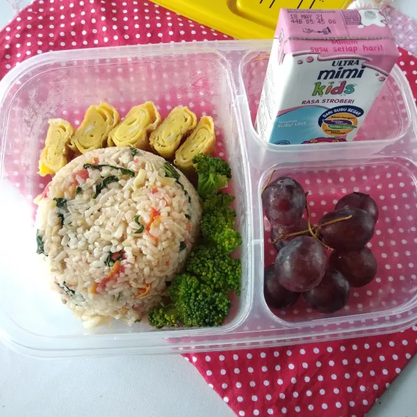 Beri potongan telur dadar, brokoli rebus, buah-buahan dan susu UHT kotak. Bento siap dibawa ke sekolah.