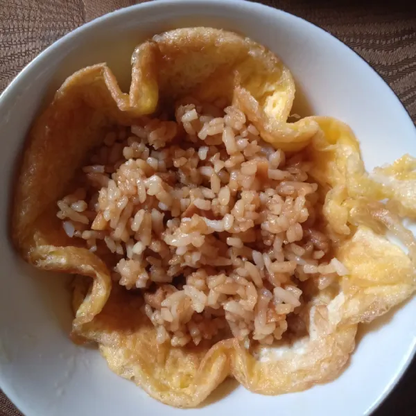 Taruh telur dadar dalam mangkok kecil, tambahkan beberapa sendok nasi goreng padatkan. Tutup dan rapikan.