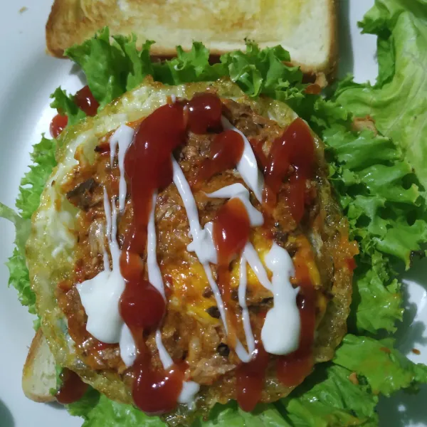 Beri saos tomat atau sambel, lalu tutup dengan roti dan belah menjadi 2 bagian.