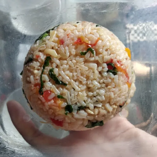 Ambil beberapa sendok nasi goreng, masukkan ke dalam mangkok, padatkan lalu balik d atas kotak bekal.