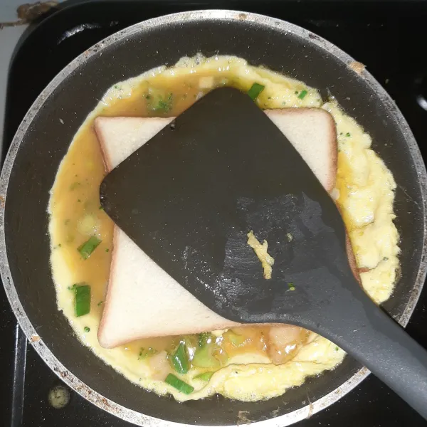 Tekan tekan dengan spatula agar roti menempel pada telur dadar. sebaiknya pakai api kecil agar telur dadar tidak terlalu cepat matang. setelah yakin menempel baru boleh besarkan apinya ke sedang. panggang hingga matang dua belah sisi. pastikan telur sudah benar-benar masak sebelum membalik ya.