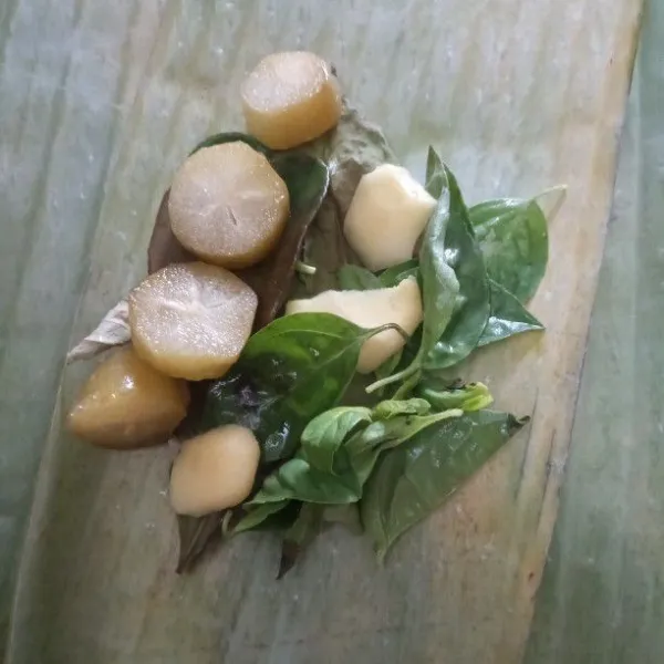 Sobek daun pisang, kemudian di atasnya tambahkan daun salam, daun jeruk, serai, jahe, kemangi, belimbing wuluh dan cabe rawit.