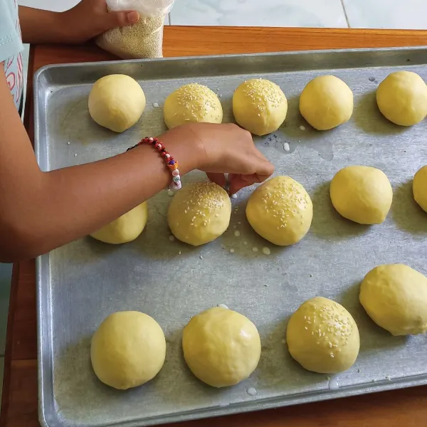 Bagi menjadi 9 buah. Bulatkan. Diamkan lagi 30 menit hingga mengembang. Olesi dengan susu cair lalu taburi dengan biji wijen.