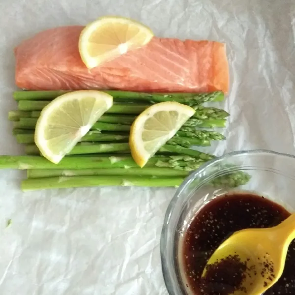 Tata asparagus dan salmon dalam loyang yang dilapisi baking paper. Beri irisan jeruk lemon diatasnya.