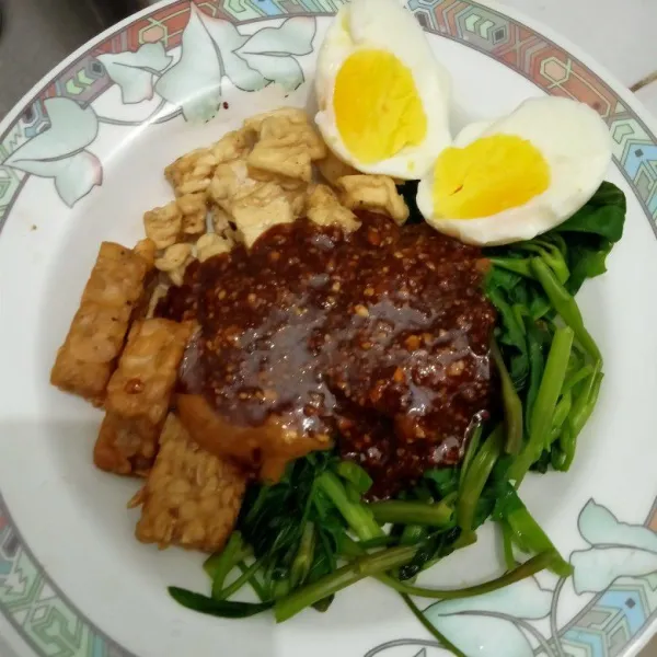 Tata di atas piring kangkung, tempe goreng, tahu goreng, telur rebus dan beri sambal kacang di atasnya.