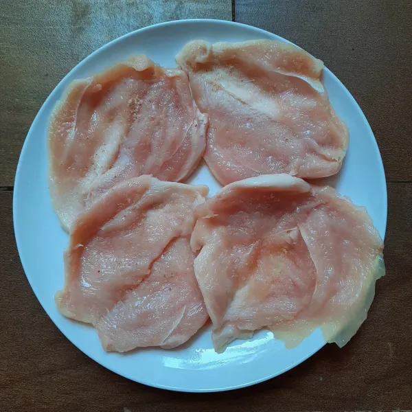 Membuat Chicken Schnitzel: belah dua dada ayam tapi tidak putus. Lumuri seluruh permukaannya dengan garam dan merica bubuk.