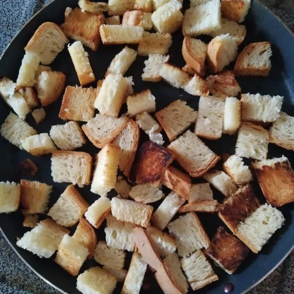 Potong-potong roti tawar membentuk dadu. Kemudian panaskan teflon dan panggang di atas kompor dengan api sedang sambil dibolak balik hingga permukaan roti garing.
