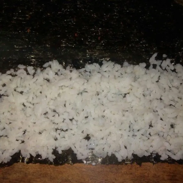 Ratakan nasi di atas selembar nori.