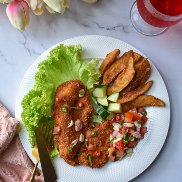 Tata Ayam goreng di atas piring, sajikan ayam Schnitzel dengan sambal dabu-dabu,dan pelengkap lainnya.