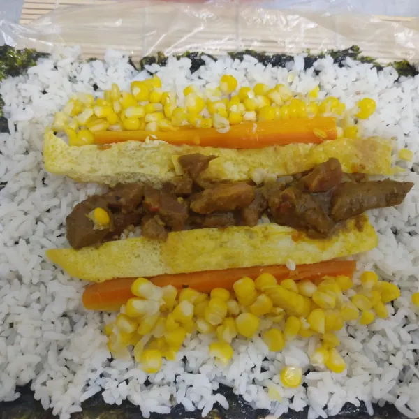 Siapkan alas sushi : letakkan rumput laut, nasi putih, jagung, telur dadar, wortel dan daging rendang kemudian gulung pelan-pelan berbentuk bulat dan potong sesuai selera.