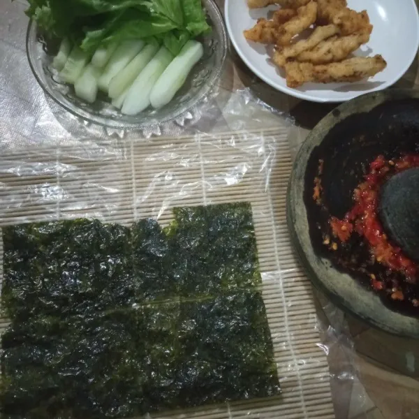 Siapkan bahan isian, potong timun memanjang. Siapkan  Sushi mat, lapisi dengan plastik tahan panas, susun nori menjadi persegi panjang.