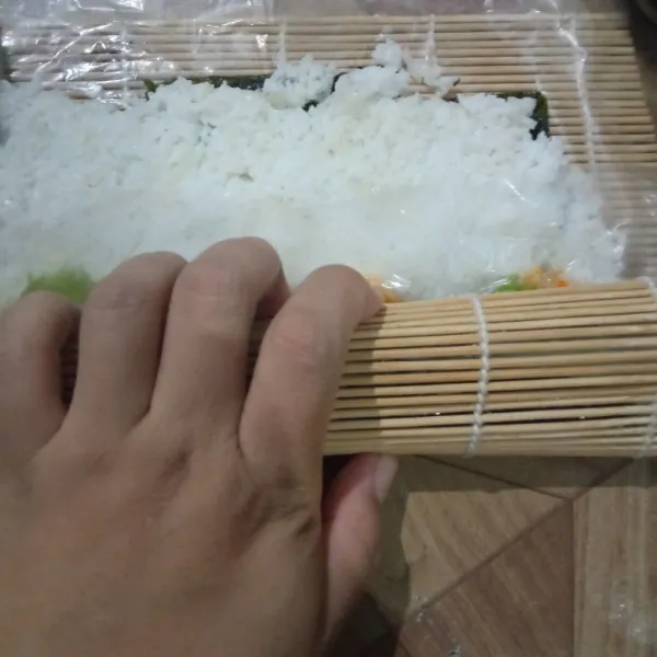 Gulung dengan Sushi mat sambil dipadatkan hingga menjadi bentuk sushi.