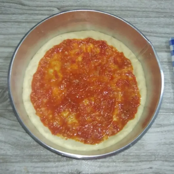 tambahkan saus tomat pada permukaan adonan pizza secara merata.