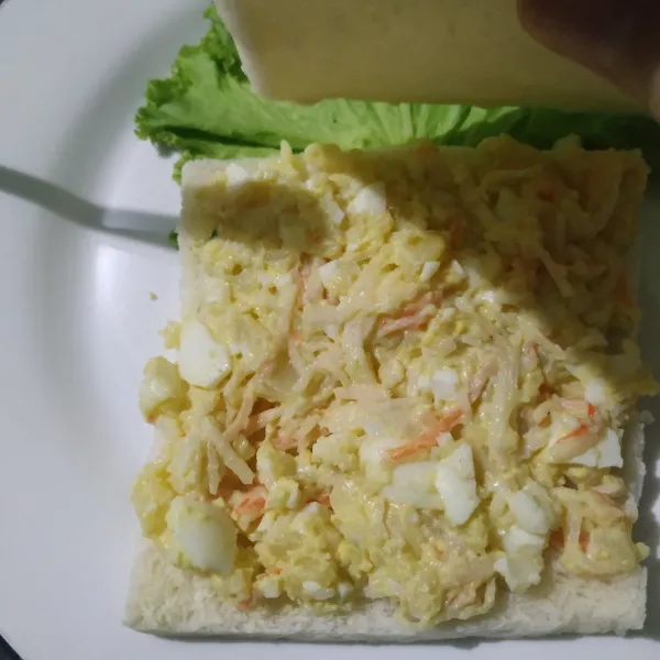 Letakan selembar roti di atasnya beri salad telur lalu tutup dengan roti lagi.