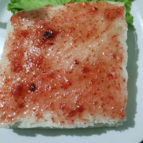 Kemudian di atas roti tadi beri selai strawberry. Lalu tutup dengan roti.