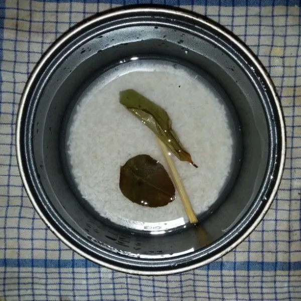 Masukkan beras, air, daun salam, daun jeruk dan batang serai ke dalam panci rice cooker.