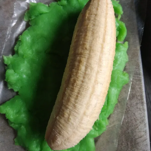 Ambil secukupnya adonan hijau, pipihkan di atas plastik kemudian letakkan pisang di atasnya.