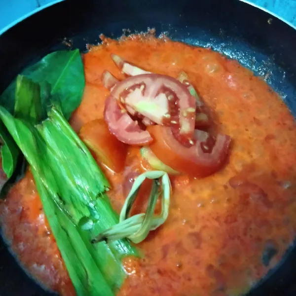 Masukkan tomat yang dipotong kecil, serai, daun kunyit, daun salam, dan daun jeruk. Aduk rata