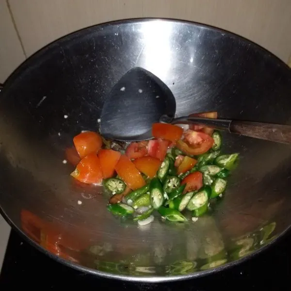 Panaskan minyak goreng. Tumis bumbu rajang, daun salam, lengkuas dan batang serai hingga harum. Masukkan irisan cabe dan tomat.