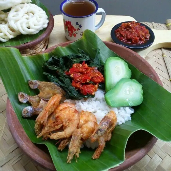 Sajikan nasi dengan lalap rebusan daun singkong dan labu siam, udang goreng, ikan asin sepat, dan sambal tomat yang pedasnya nampol.