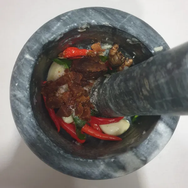 Tumbuk halus bawang putih, cabai rawit merah, dan daun Jeruk purut yang telah digoreng tadi. Masukkan garam halus, terasi bakar, gula merah, kencur, dan asam Jawa. Tumbuk/ulek sampai lumat