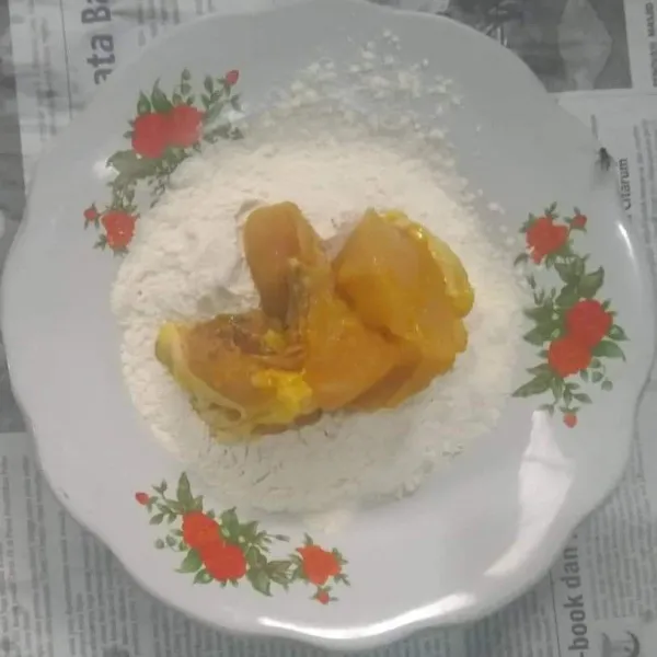 Tuang tepung bumbu serbaguna ke dalam piring, masukkan potongan daging ayam.