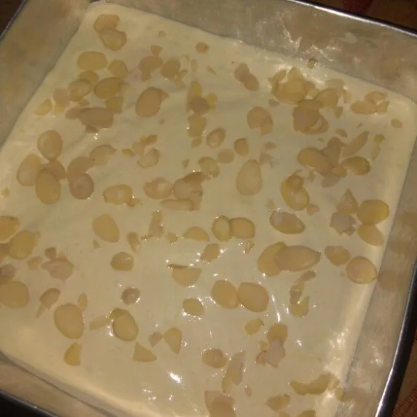 Tuang adonan dalam loyang yang sudah dioles margarin dan kertas roti, lalu beri topping almond slice