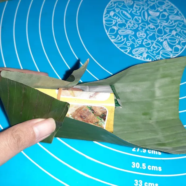 Untuk mempermudah, buat cetakan dulu dari kardus (saya pakai kardus kue) dibentuk jadi limas. Lalu bentuk daun pisang mengikuti cetakan.