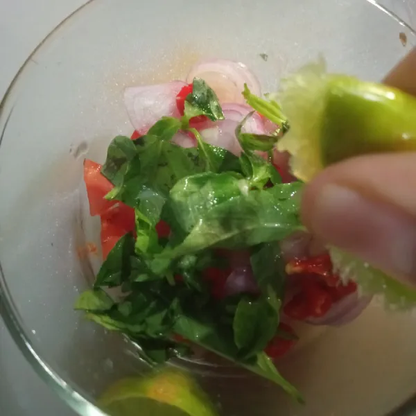 Masukkan tomat, cabe, dan bawang ke dalam wadah, tambahkan daun kemangi, lalu beri air perasan jeruk nipis.