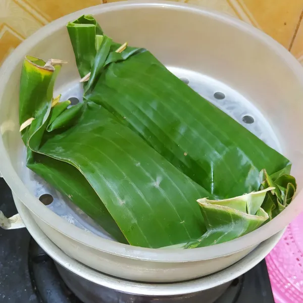 Ambil secukupnya daun pisang lalu letakkan 2 lembar daun salam. Tambahkan satu ekor ikan beserta bumbu. Gulung dan sematkan lidi di kedua sisinya. Kukus selama 45 menit.