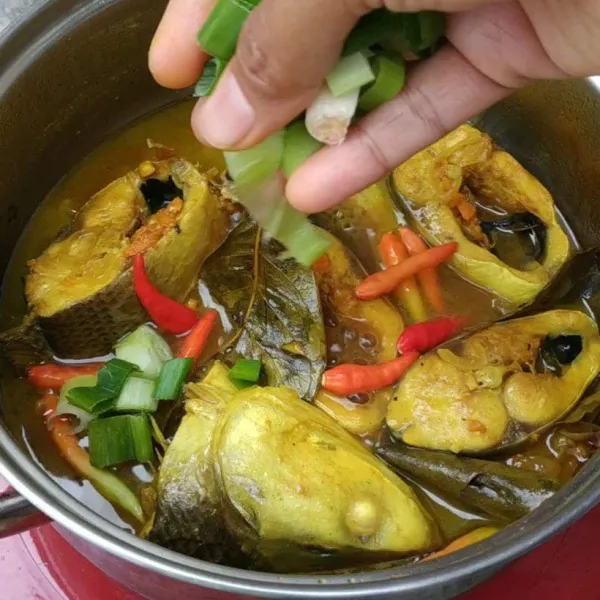 Masak ikan sampai menguning dan air mulai mengental, lalu masukkan cabai utuh dan daun bawang