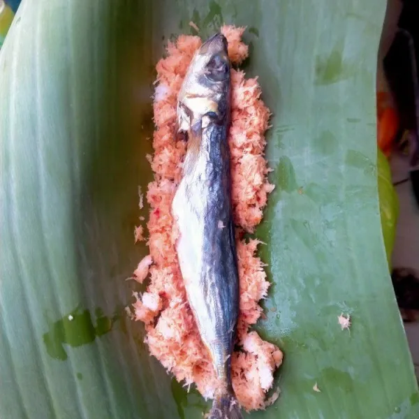 Setelah itu ambil daun pisang, masukkan parutan kelapa muda. Taruh ikan diatasnya kemudian bungkus, tusuk dengan lidi