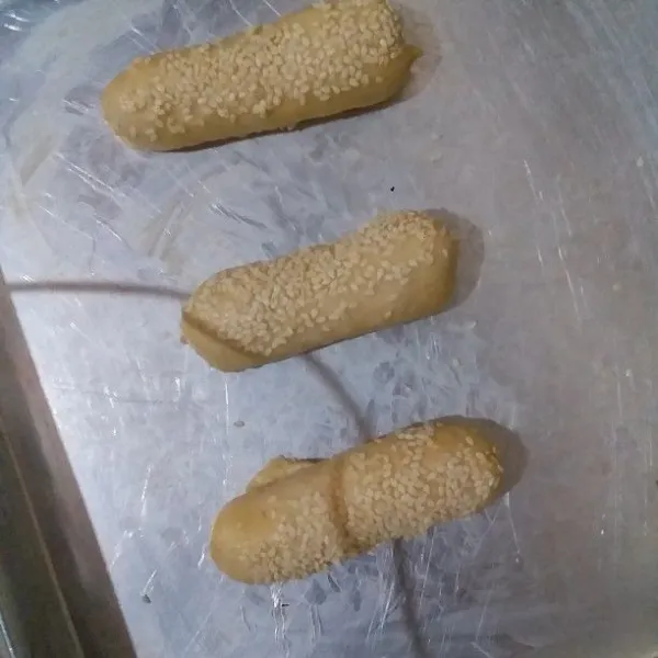 Untuk adonan Hotdog. Timbang adonan @ 45 gr. Bulatkan dan pipihkan dengan rolling pin kemudian gulung. Oleskan permukaan adonan dengan air lalu taburkan wijen