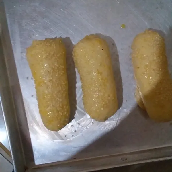 Tutup adonan dengan serbet. Diamkan adonan selama 60 menit. Setelah mengembang oleskan permukaan adonan dengan campuran kuning telur dan susu cair