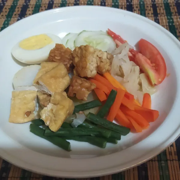 Tata di piring, irisan lontong, tahu, tempe, kentang, telur, dan sayuran.