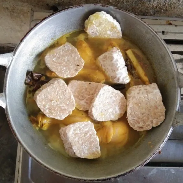 Masukkan tempe setelah air pada ungkepan ayam berkurang.