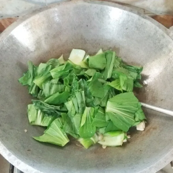 Tambahkan air ke dalam tumisan. Masukan daun pakcoy. Aduk rata. Tutup lagi wajannya hingga daun pakcoy layu.