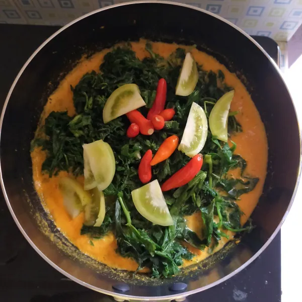 Setelah mengental dan mendidih, masukan daun singkong, tomat hijau dan cabe rawit merah ke dalam kuah lalu aduk hingga merata.